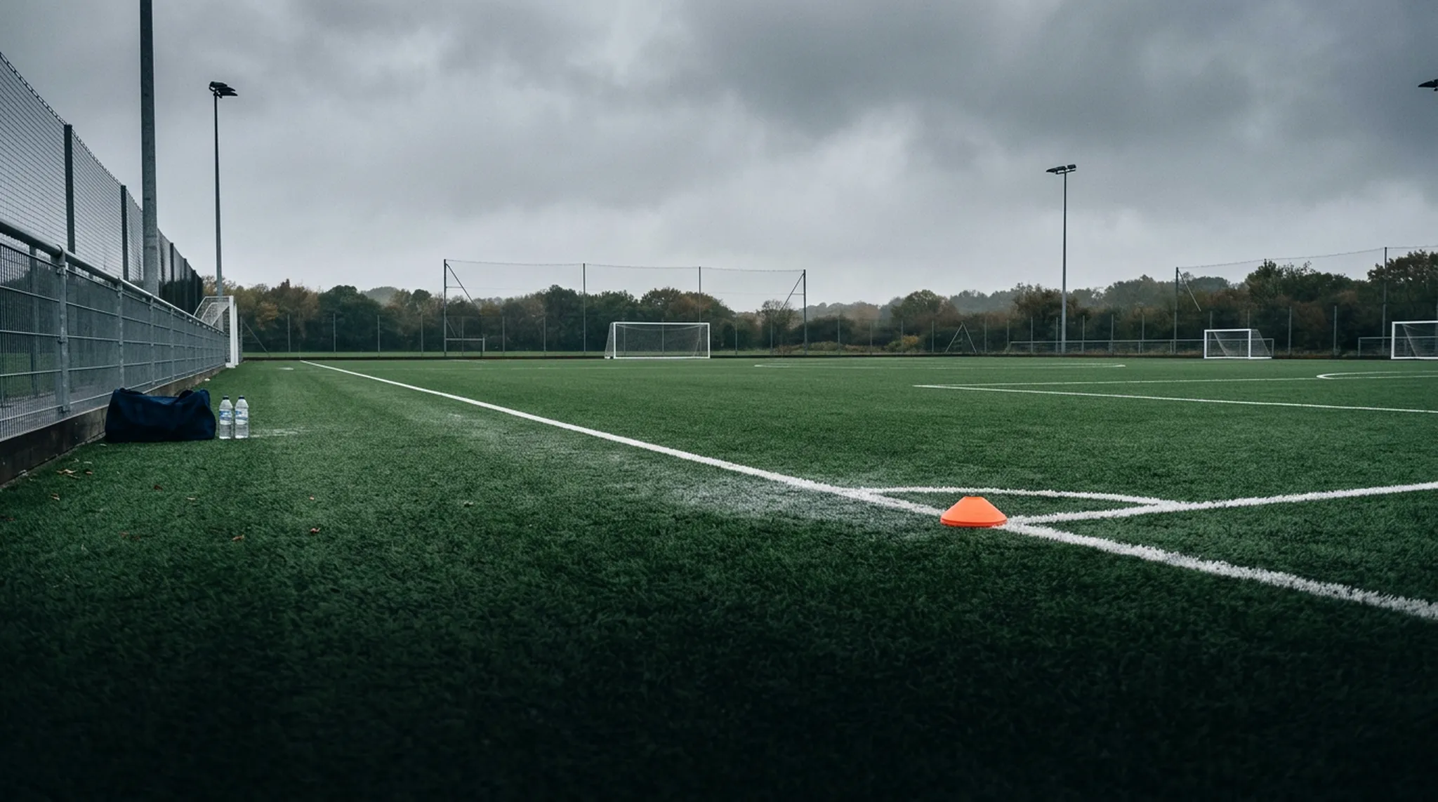 A training cone on an empty grassroots pitch under floodlights